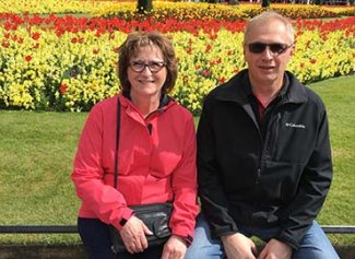 Photo of Mona and her husband sitting in a garden with bright flowers
