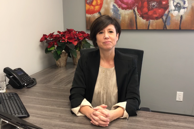 Erin sitting at a desk with her hands folded and a red poinsettia behind her.