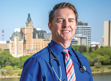 Dr. Adamko standing infront of the Delta Bessborough smiling in a blue shirt with his stethescope on